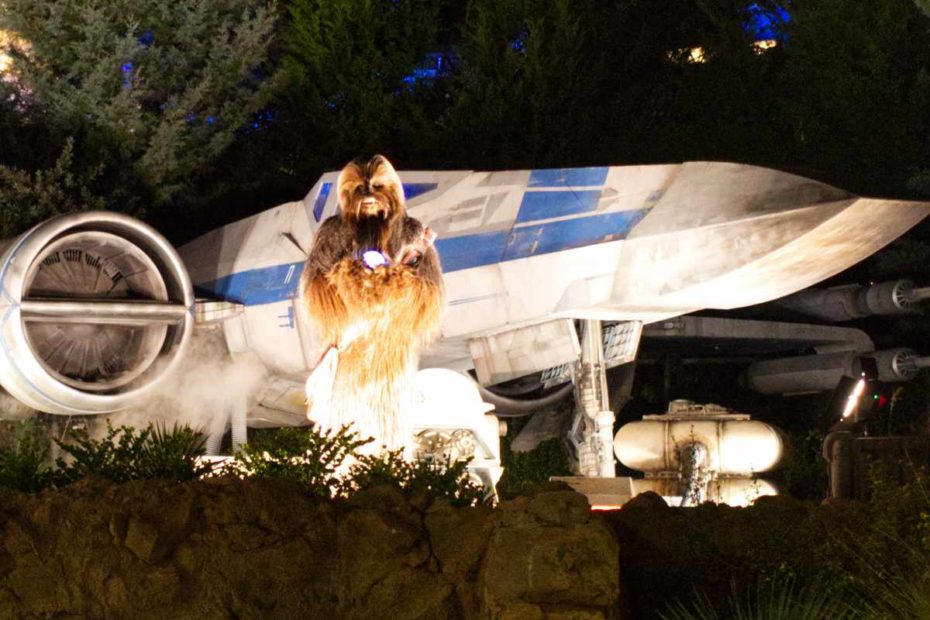 Chewbacca holding a Life Day orb in front of the X-Wing inside Star Wars: Galaxy's Edge